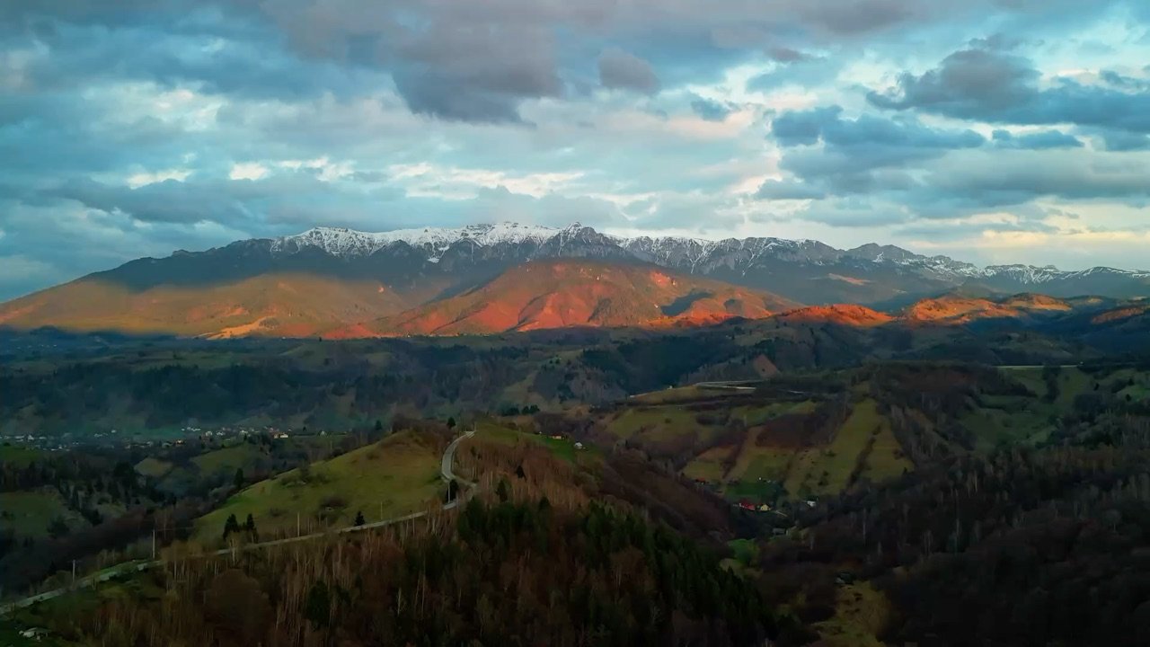 Crestele munților luminate de apus, deasupra dealurilor împădurite