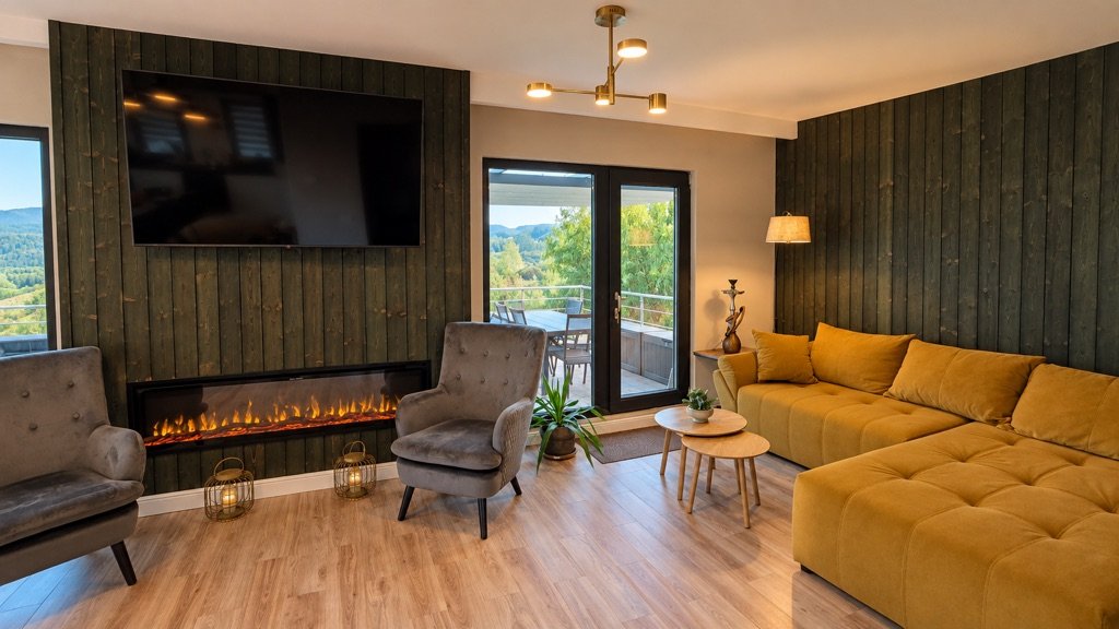 Canapeaua muștar din living, cu șemineu electric și ușă spre terasă